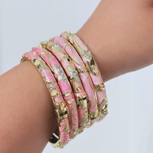K&ouml;nnte beinhalten: Ein Set aus vier aufklappbaren Armreifen in Goldoptik mit rosa und hellgr&uuml;nen Emaille-Blumenmustern und eingelassenen klaren Kristallen. Jeder Armreif verf&uuml;gt &uuml;ber einen sicheren Metallverschluss und eine polierte Oberfl&auml;che.