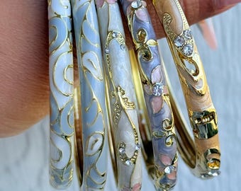 May include: Set of six decorative bangles in various colors, including light blue, white, and gold. The bangles feature floral and swirl designs with rhinestone accents. The text "Set 8" is in the upper left corner.