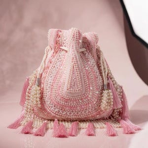 May include: A pink beaded drawstring bag with white and pink pearl accents. The bag features a detailed pattern of beads and sequins, with white rope drawstrings and pink tassels. The bag is a stylish accessory.