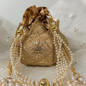 May include: A gold-coloured, beaded drawstring pouch with intricate embroidery and a floral design. The pouch is adorned with multiple strands of faux pearls and gold-coloured chain accents, creating an elegant, ornate look.
