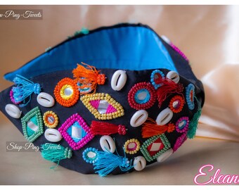 May include: A black headband with colorful beads, mirrors, and seashells. The headband is decorated with tassels in various colors, including orange, pink, blue, and green.
