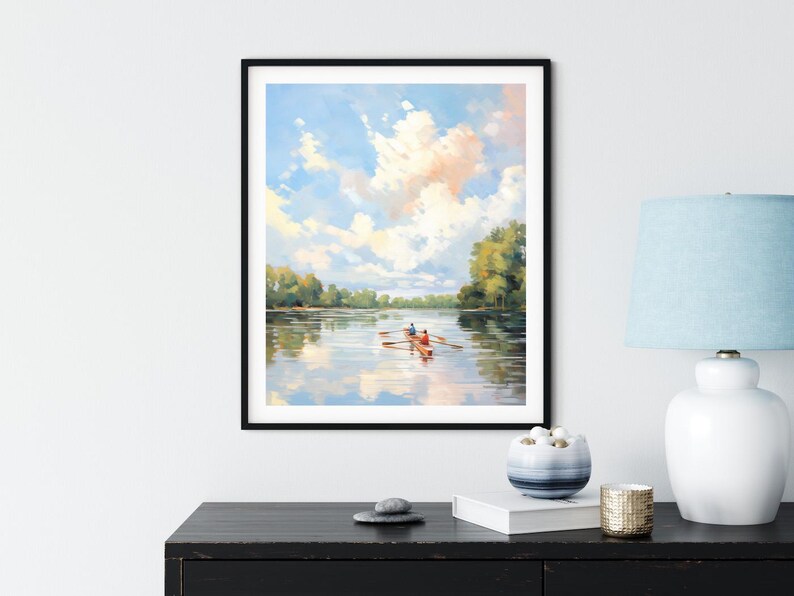 May include: A framed painting depicts a serene river scene with a rowboat carrying two people. The sky is filled with fluffy clouds, reflecting in the water. The artwork is framed in a black frame and displayed on a black surface.