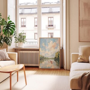 May include: A framed landscape painting featuring a serene river scene with two people in a rowboat under a cloudy sky. The artwork is displayed in a living room with a neutral color palette, a wooden floor, and large windows.