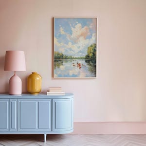 May include: A framed landscape painting depicts a serene river scene with a boat and two figures. A light blue cabinet with a pink lamp and yellow vase sits below the painting. The room has pink walls and a light blue baseboard.