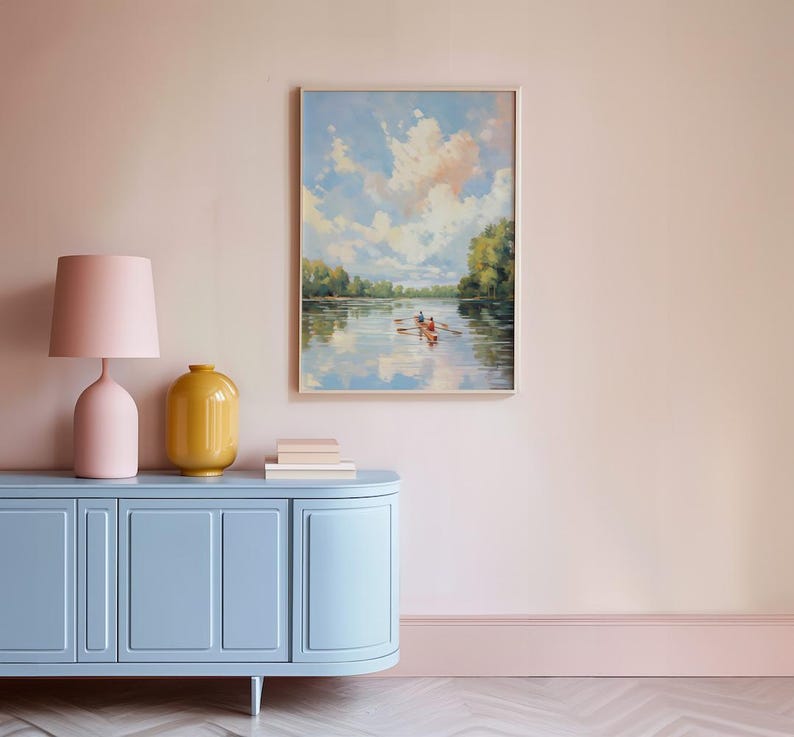 May include: A framed landscape painting depicts a serene river scene with a boat and two figures. A light blue cabinet with a pink lamp and yellow vase sits below the painting. The room has pink walls and a light blue baseboard.