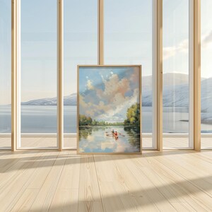 May include: A framed landscape painting depicts a serene river scene with a rowboat and two figures. The artwork features a cloudy sky with soft pink and blue hues, reflected in the water. The frame is a light wood color, and the painting is displayed on a wooden floor.
