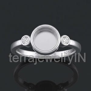 May include: A silver ring with a large, round bezel setting in the center, flanked by two smaller round settings with clear stones. The ring is stamped with "925" and the text "terrajewelryIN".