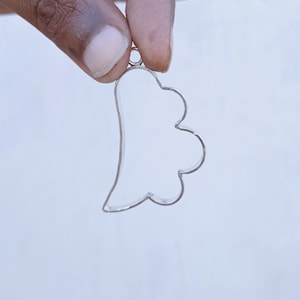 May include: A silver metal pendant shaped like a cloud with a loop at the top for attaching a chain.