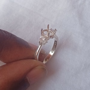 Peut inclure: Une bague en argent avec trois pierres transparentes, une ronde et deux en forme de poire. La bague est marquée "925" à l'intérieur de la bande.