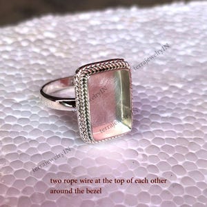 Op de afbeelding: Zilveren ring met een rechthoekige bezel met een touwdraadontwerp rond de rand. De bezel is leeg en klaar om te worden gevuld met een steen of ander materiaal.
