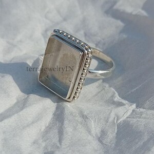 Op de afbeelding: Een zilveren ring met een vierkante zetting. De zetting is versierd met een rij kleine kralen. De ring is ontworpen om een ​​edelsteen of ander materiaal te bevatten.