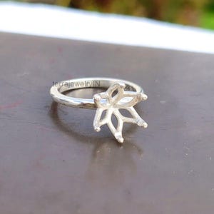 May include: A silver ring with a floral design. The ring features a detailed, openwork flower setting, and the band is smooth and polished. The ring is set against a neutral background, highlighting its intricate design. The text "terrajewelryIN" is visible on the ring.