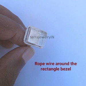 Op de afbeelding: Een zilveren ring met een vierkante bezel. De bezel is omgeven door een touwdraadontwerp. De tekst "terrajewelryIN" is zichtbaar in de bezel.