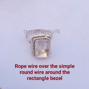 Op de afbeelding: Zilveren ring met een rechthoekige bezel. De bezel is omgeven door een touwdraadontwerp.