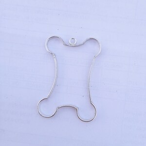 May include: Silver metal pendant shaped like a bone with a small loop at the top for attaching a chain.