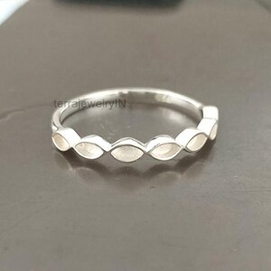 May include: A silver ring with a repeating pattern of oval-shaped settings. The ring is set against a dark gray background. The text "terrajewelryIN" is visible on the ring.