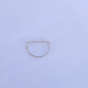 May include: A silver pendant with a half-circle design. The pendant has a straight top with two small loops for a chain and a curved bottom. The metal has a textured appearance.
