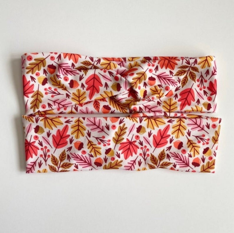 Puede incluir: Un par de diademas de tela blanca con un estampado de oto&ntilde;o de hojas rojas, naranjas y amarillas, bellotas y bayas.