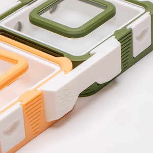 Pode incluir: Um conjunto de três recipientes de plástico com tampas. O recipiente superior é verde, o recipiente do meio é branco e o recipiente inferior é laranja.