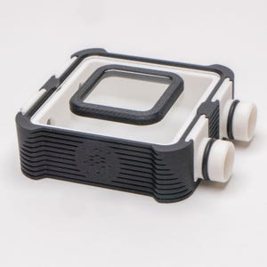 Puede incluir: Un depósito de refrigeración por agua impreso en 3D blanco y negro con dos puertos de tubo transparentes. El depósito tiene una ventana transparente en la parte superior.