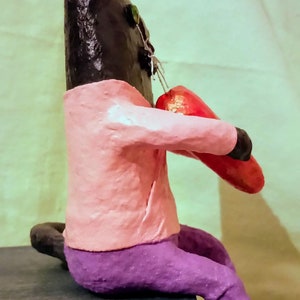 May include: A black cat figurine wearing a pink shirt and purple pants, holding a red heart in its paws.