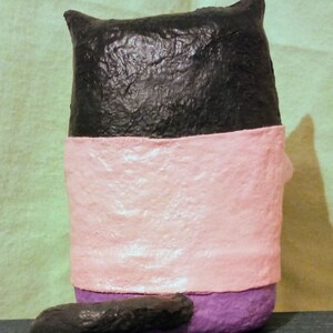 May include: A black, pink, and purple handmade cat figurine. The cat is sitting with its tail curled behind it.