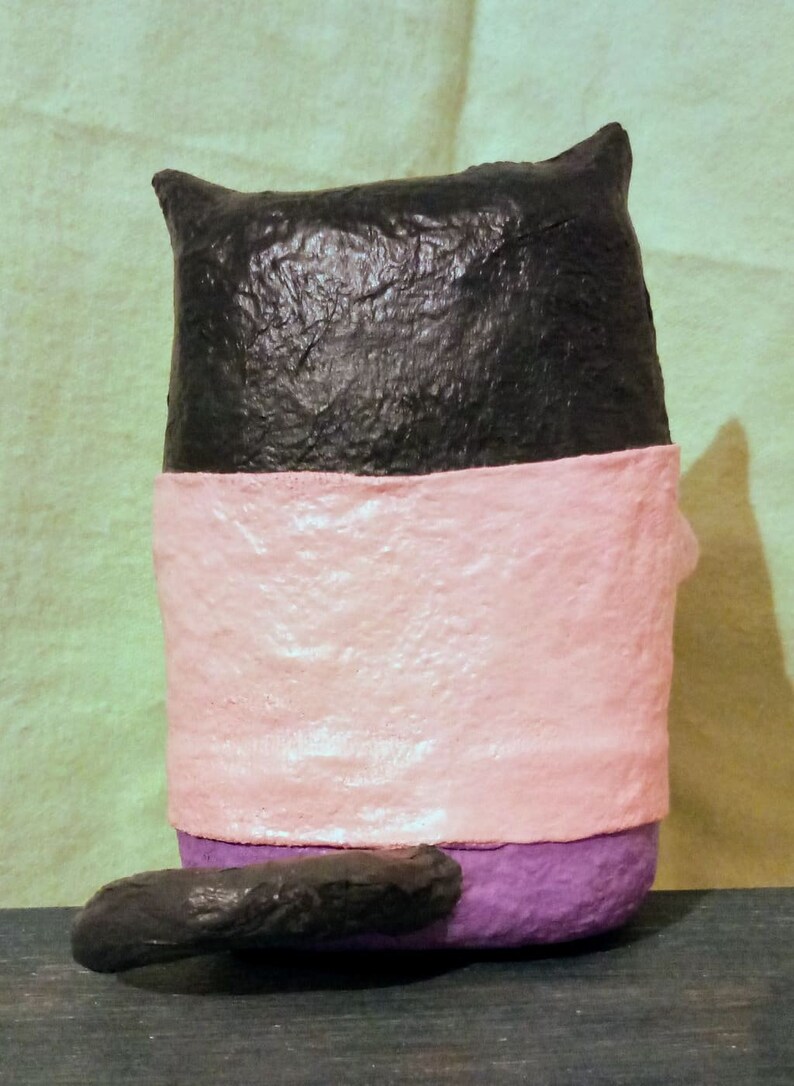 May include: A black, pink, and purple handmade cat figurine. The cat is sitting with its tail curled behind it.