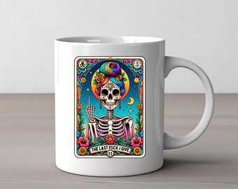 May include: White ceramic mug featuring a colorful illustration of a skeleton with rainbow hair and floral accents. The image includes the text "THE LAST FUCK I GIVE" and is framed with decorative elements.