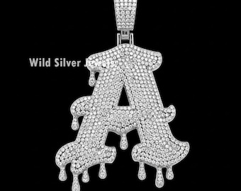 May include: A silver pendant in the shape of the letter A, with a dripping design. The pendant is covered in small, clear stones.