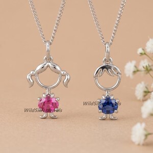 Peut inclure: Deux colliers pendentifs en argent. Un pendentif représente une fille avec une pierre précieuse rose, l'autre un garçon avec une pierre précieuse bleue. Les deux pendentifs ont une tête circulaire et un corps avec des pieds.
