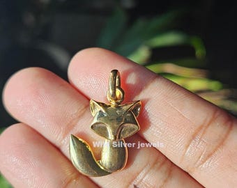 Könnte beinhalten: Ein goldfarbener Fuchsanhänger mit einer Schlaufe für eine Kette. Der Fuchs sitzt mit aufgerolltem Schwanz. Der Anhänger hat eine glatte, polierte Oberfläche. Der Text "W Silver jewels" ist sichtbar.