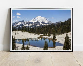 May include: A scenic photograph of a mountain lake with a snow-capped mountain in the background. The lake is surrounded by evergreen trees and snow-covered ground.