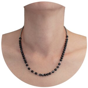 May include: A black and white beaded necklace with a silver chain. The necklace is made of round beads with a black and white marbled pattern.