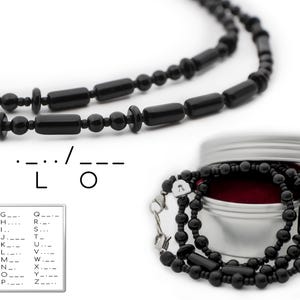 Könnte beinhalten: Schwarze Perlenkette mit einem silbernen Verschluss. Die Kette besteht aus runden und rechteckigen Perlen. Die Kette liegt auf einer weißen Oberfläche. Der Morsecode für "LO" ist unterhalb der Kette abgebildet.