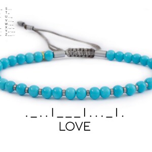 May include: Turquoise beaded bracelet with silver accents. The bracelet features the word "LOVE" in Morse code. The adjustable cord is gray. A chart of Morse code letters is in the upper left corner.