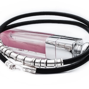 May include: A black leather cord necklace with a silver clasp and a row of silver beads. The necklace is lying on a white surface with a clear glass bottle of pink lip gloss.