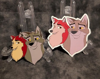 May include: Two enamel pins featuring the characters from the animated film "Balto". The pins are of Balto and Jenna, the wolf-dog and the female dog, respectively. The pins are on a clear plastic stand.