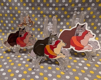 May include: Three metal keychains featuring a cartoon couple of dogs. The dogs are brown, black, and white with red and orange accents. The keychains are on a gray and white polka dot background.