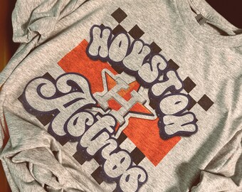 May include: Gray long-sleeve t-shirt with a blue and orange graphic print that says "Houston Astros" with a star and a baseball bat.