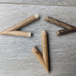 Peut inclure: Quatre pointes de flèche en bois avec des pointes pointues, deux sont brun clair et deux sont brun foncé. Les pointes de flèche sont disposées en forme d'étoile sur une surface en bois clair.