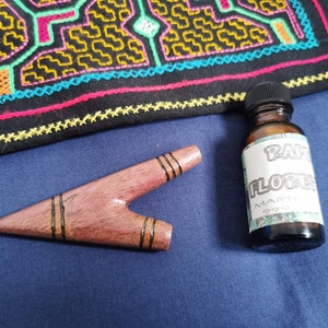 Puede incluir: Una pequeña pipa de madera con una mancha marrón oscura y líneas negras. Una pequeña botella con una etiqueta blanca que dice "Rapa Flores Martin 999" está al lado de la pipa.