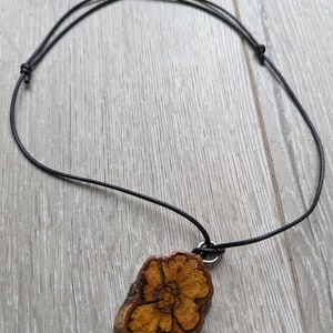 May include: A wooden pendant necklace with a black cord. The pendant is a natural wood slice with a burnt flower design.