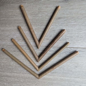 Peut inclure: Un ensemble de sept bâtonnets en bois brun disposés en forme de V sur une surface en bois brun clair.