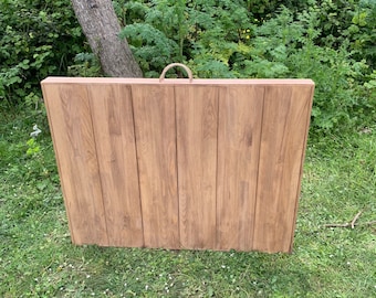 May include: A wooden folding table with a rope handle. The table is closed and has a natural wood finish.