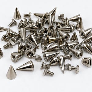 Può includere: Una collezione di punte coniche in metallo color argento con viti posteriori filettate abbinate. Ogni punta presenta una sommità appuntita e una base circolare piatta con un foro centrale, mentre le viti hanno teste piatte e gambi filettati.