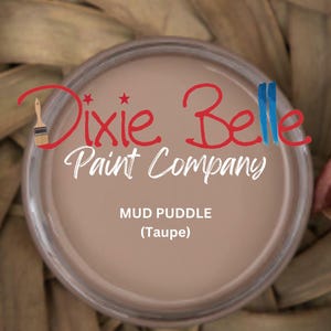 May include: A jar of "Mud Puddle" (Taupe) paint from Dixie Belle Paint Company. The paint is a light brown color. The Dixie Belle logo is in red and white script. The jar is set against a woven background.