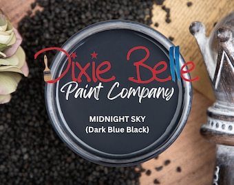May include: A round container of Dixie Belle Paint Company paint in the color Midnight Sky, described as Dark Blue Black. The label features the brand name in red and white text, with the color name printed clearly in white on the dark paint surface.