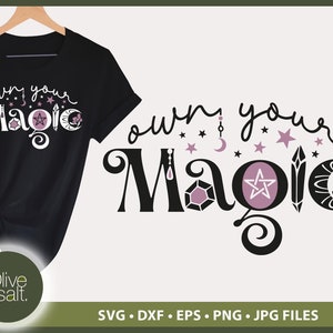 Könnte beinhalten: Ein schwarzes T-Shirt mit dem Text "own your magic" in rosa und schwarzer Schrift. Der Text ist von Sternen, Monden und Kristallen umgeben. Der Text "Olive & salt." befindet sich in einem Kreis am unteren Rand des Bildes.