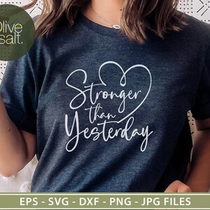 Pu&ograve; includere: Una maglietta blu scuro con un cuore bianco e il testo "Stronger than Yesterday" stampato sul davanti.