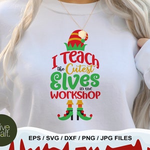 May include: White sweatshirt with a green, red, and yellow elf hat and the text "I Teach the Cutest Elves in the Workshop".  The elf hat has a red pom-pom and the text is in a festive font.  The sweatshirt also has two green elf shoes with red and yellow accents.